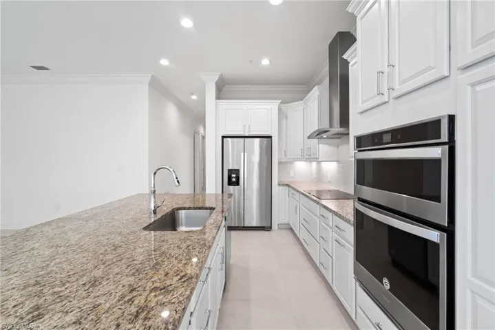 Kitchen with crown molding, wall chimney range hood, stainless steel appliances, decorative backsplash, and sink