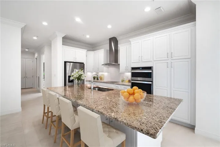 Kitchen with appliances with stainless steel finishes, sink, light stone counters, white cabinetry, and wall chimney exhaust hood
