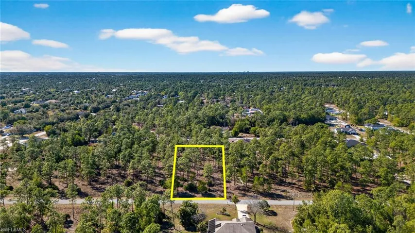Aerial view of property and surrounding area with property parcel outlined and a heavily wooded area