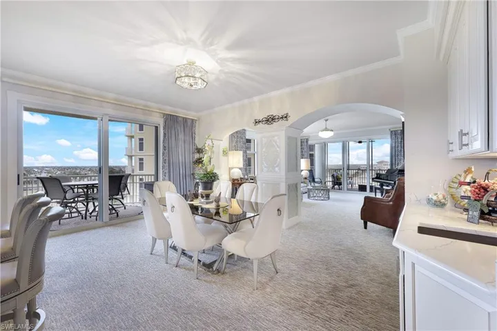 Dining area with arched walkways, light carpet, crown molding, and a chandelier