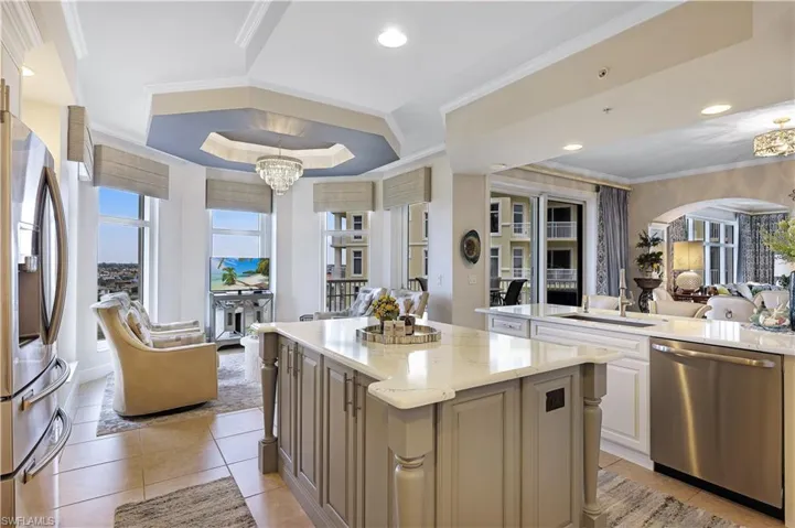 Kitchen with open floor plan, ornamental molding, a raised ceiling, light stone counters, and appliances with stainless steel finishes
