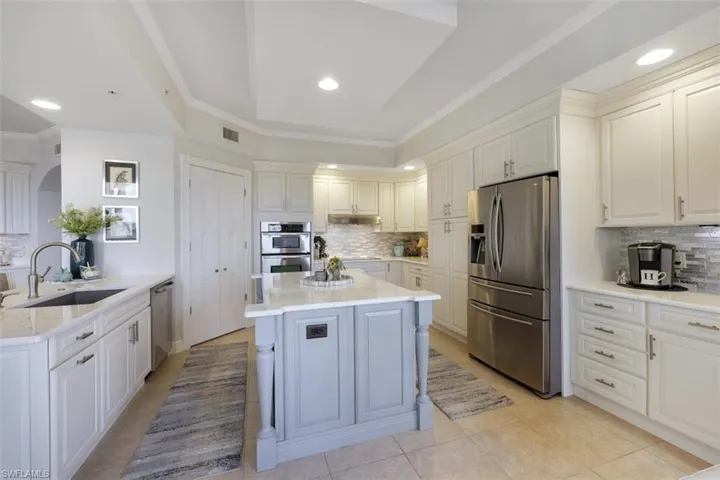 Kitchen featuring crown molding, appliances with stainless steel finishes, tasteful backsplash, light stone counters, and light tile patterned floors