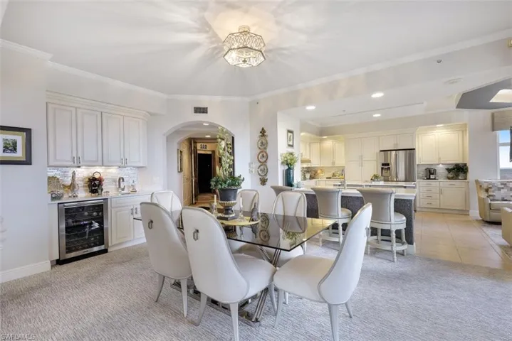 Dining room with arched walkways, wine cooler, recessed lighting, light tile patterned floors, and light carpet