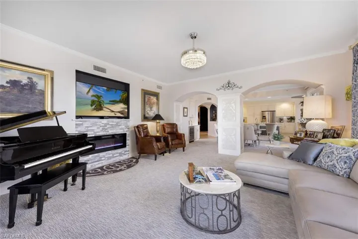 Living area featuring arched walkways, ornamental molding, carpet floors, a chandelier, and a fireplace