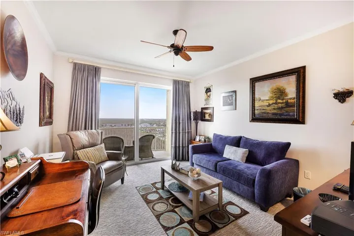 Carpeted living room featuring ornamental molding, ceiling fan, and an office area
