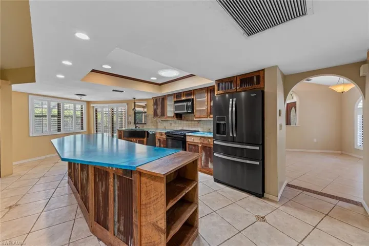 Kitchen featuring light tile flooring, decorative backsplash, dark stainless appliances, and a raised ceiling