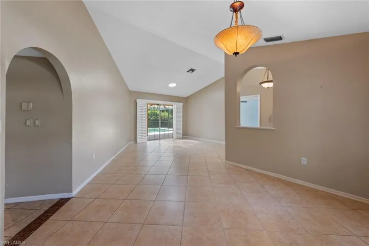 Dining room looking into living room, featuring light tile floors and vaulted ceiling