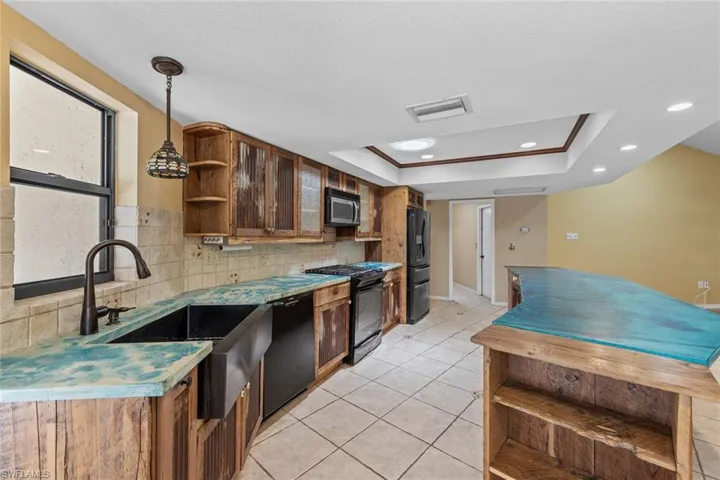 Kitchen with dark stainless appliances, decorative backsplash, a raised ceiling, and light tile floors