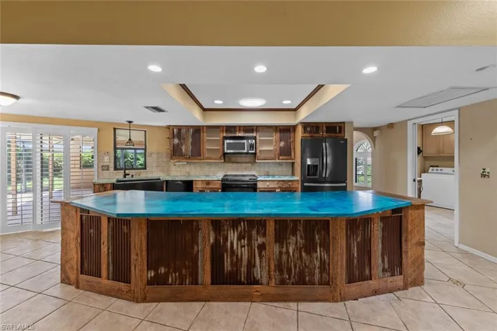 Kitchen featuring light tile flooring, decorative backsplash, dark stainless appliances, and a raised ceiling