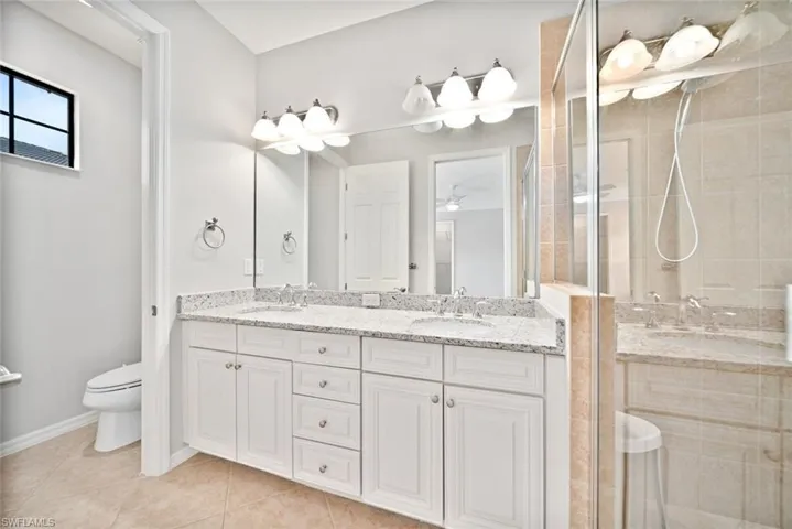 Bathroom with toilet, tile patterned floors, a shower with shower door, dual bowl vanity, and ceiling fan
