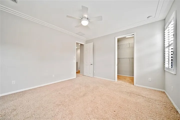 Unfurnished bedroom with a walk in closet, ceiling fan, multiple windows, and light colored carpet
