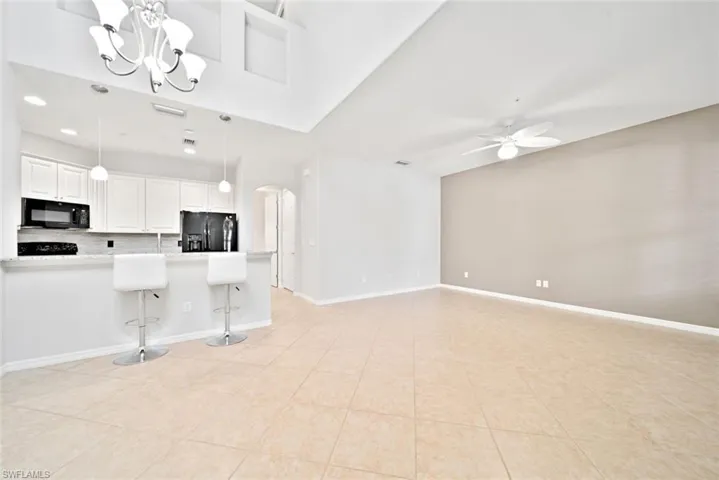 Kitchen with backsplash, black appliances, pendant lighting, light tile patterned floors, and a breakfast bar area