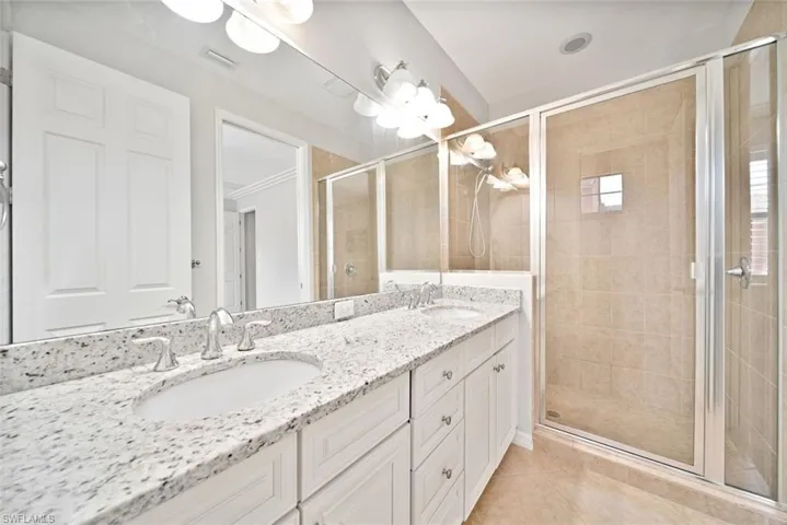 Bathroom with a shower with shower door, double vanity, ornamental molding, and tile patterned flooring