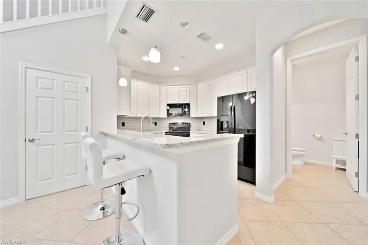 Kitchen with light stone counters, decorative backsplash, kitchen peninsula, pendant lighting, and black appliances