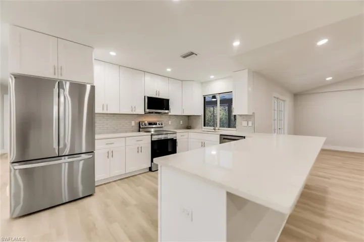 Kitchen featuring appliances with stainless steel finishes, kitchen peninsula, white cabinets, light hardwood / wood-style floors, and backsplash