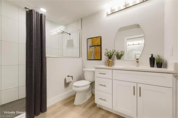 Virtually staged Bathroom with hardwood / wood-style flooring, vanity, a tile shower, and toilet