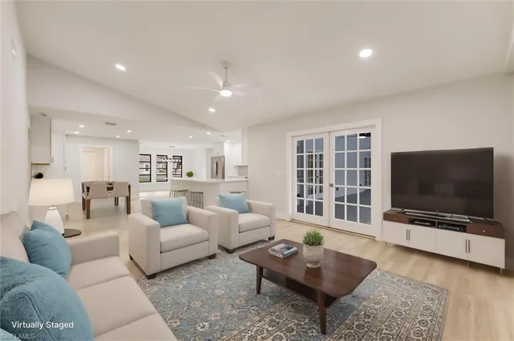 Virtually staged Living room with vaulted ceiling, light hardwood / wood-style floors, french doors, and ceiling fan