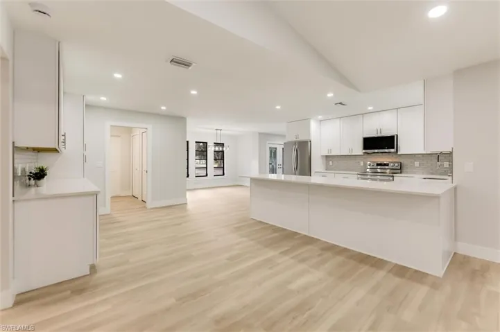Kitchen featuring white cabinetry, kitchen peninsula, stainless steel appliances, light hardwood / wood-style floors, and backsplash