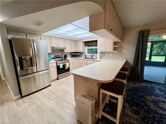 Kitchen with a healthy amount of sunlight, appliances with stainless steel finishes, kitchen peninsula, and luxury vinyl plank floors.