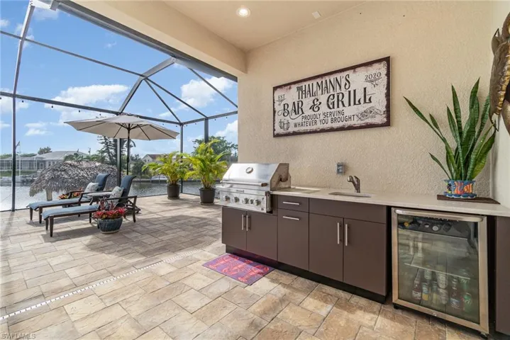 View of patio featuring a water view, a lanai, a grill, exterior kitchen, and beverage cooler