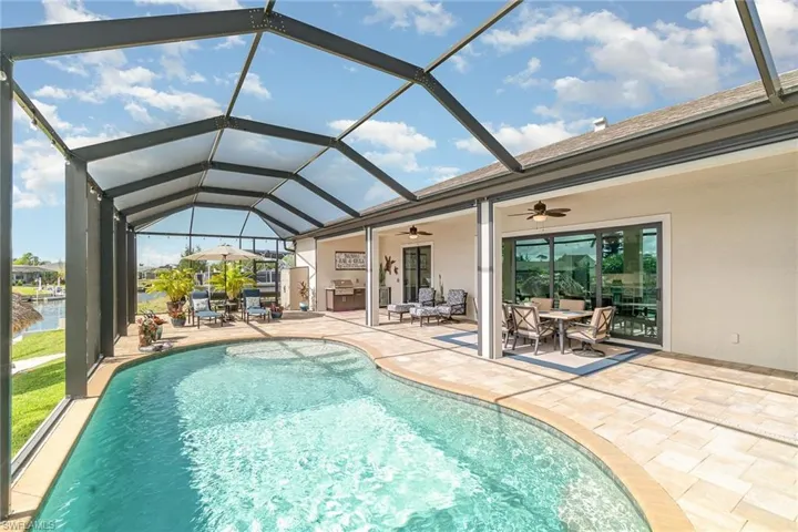 View of swimming pool with a lanai, a water view, ceiling fan, and a patio area