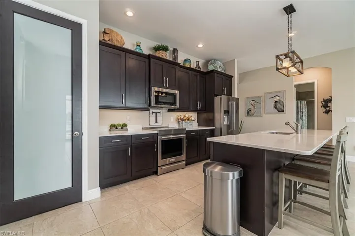 Kitchen featuring sink, an island with sink, appliances with stainless steel finishes, decorative light fixtures, and a kitchen bar