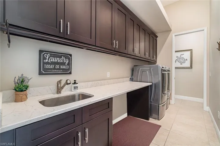 Washroom featuring washing machine and clothes dryer, sink, light tile patterned floors, and cabinets