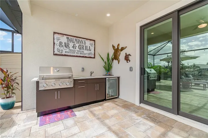 View of patio featuring a lanai, beverage cooler, exterior kitchen, sink, and a grill
