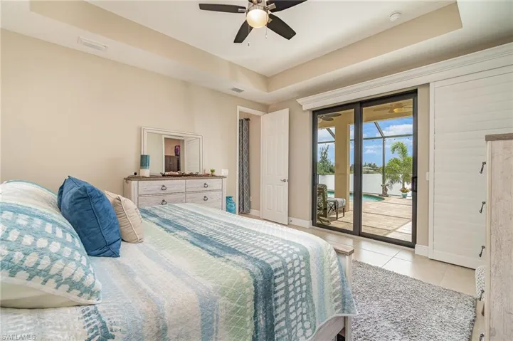 Tiled bedroom with ceiling fan, a raised ceiling, and access to outside