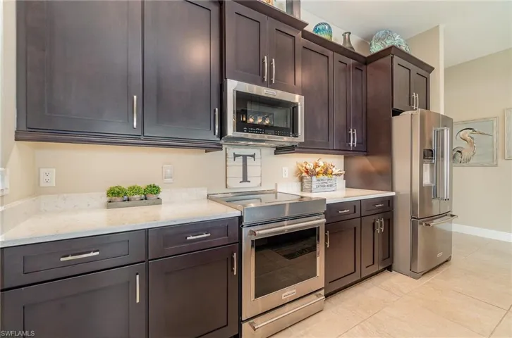Kitchen featuring dark brown cabinetry, light stone countertops, light tile patterned floors, and stainless steel appliances
