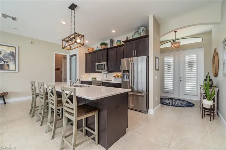 Kitchen featuring dark brown cabinetry, sink, hanging light fixtures, stainless steel appliances, and an island with sink
