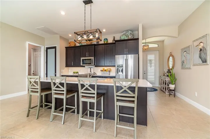 Kitchen featuring dark brown cabinetry, pendant lighting, a kitchen bar, a center island with sink, and appliances with stainless steel finishes