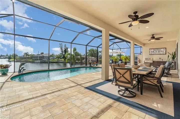 View of pool with a water view, area for grilling, glass enclosure, and a patio area