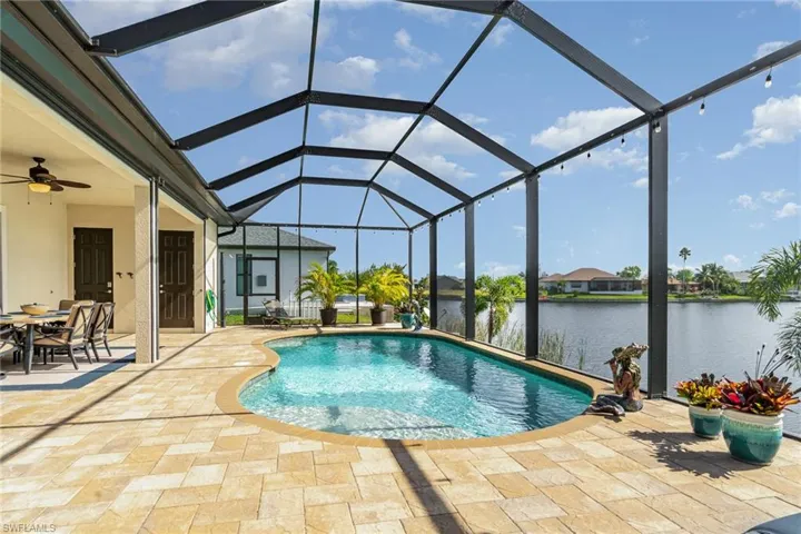 View of swimming pool featuring glass enclosure, a patio area, a water view, and ceiling fan