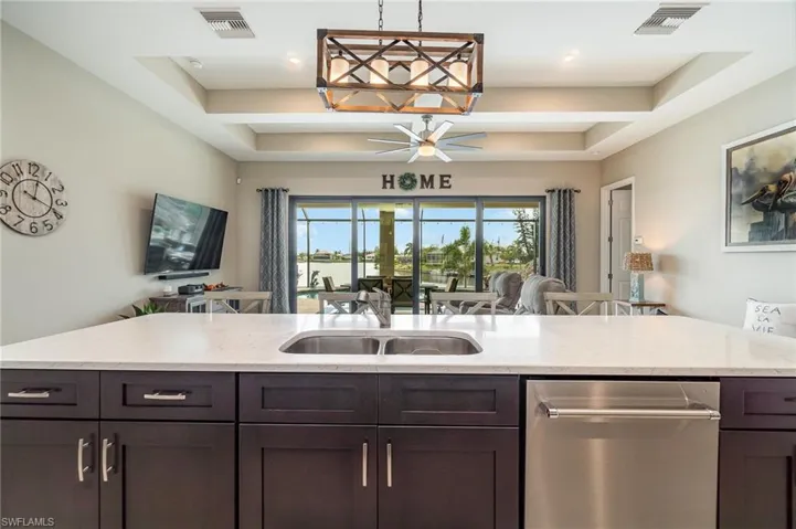 Kitchen featuring a raised ceiling, ceiling fan, dark brown cabinets, and light stone countertops