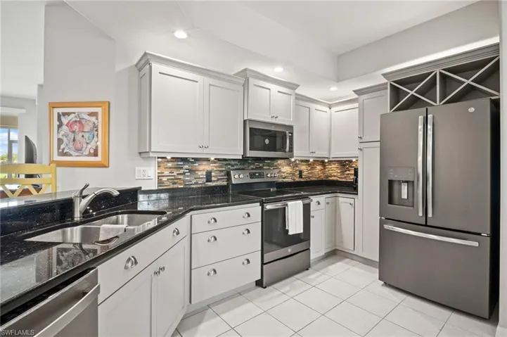 Kitchen featuring appliances with stainless steel finishes, a sink, backsplash, light tile patterned floors, and dark stone counters