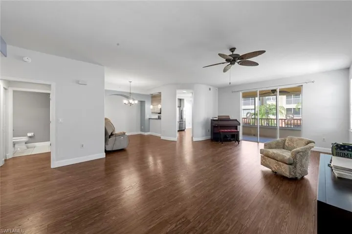 Living area featuring ceiling fan with notable chandelier, baseboards, and wood finished floors
