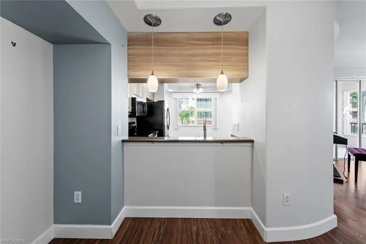 Kitchen featuring wood finished floors, freestanding refrigerator, a wealth of natural light, stainless steel microwave, and decorative light fixtures