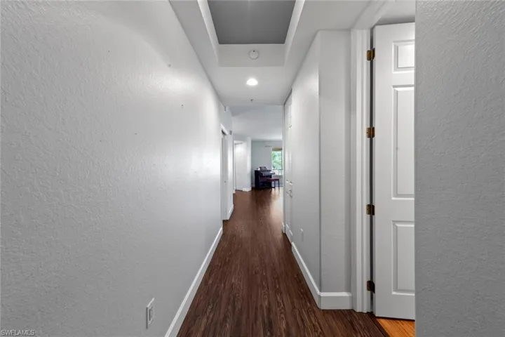 Hallway featuring recessed lighting, a textured wall, baseboards, and wood finished floors