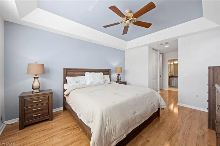 Bedroom featuring light wood-type flooring, visible vents, baseboards, and a raised ceiling