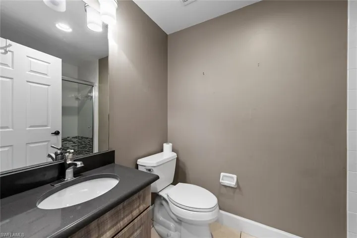 Bathroom featuring a shower with door, toilet, baseboards, tile patterned floors, and vanity