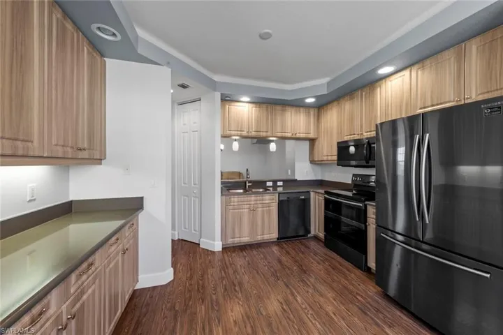 Kitchen with black appliances, dark countertops, dark wood finished floors, and a sink