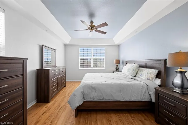 Bedroom featuring a tray ceiling, light wood finished floors, baseboards, and ceiling fan