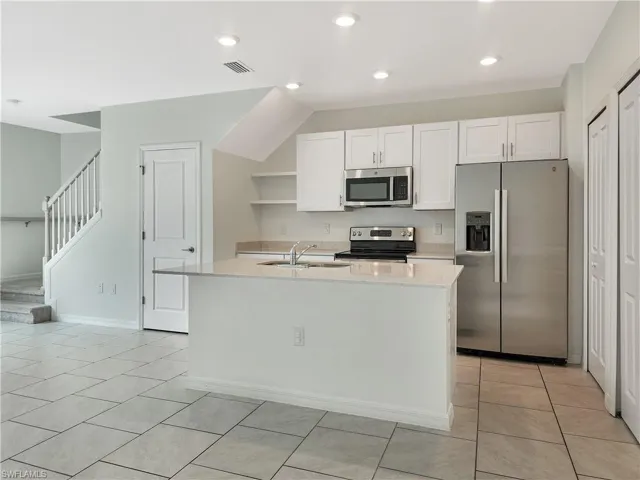 Kitchen featuring a kitchen island with sink, white cabinets, sink, appliances with stainless steel finishes