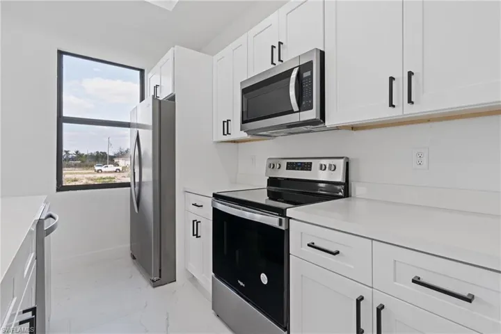 Kitchen with stainless steel appliances, light marble finish floors, light countertops, and white cabinets