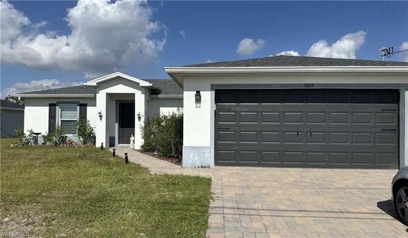 Ranch-style house featuring decorative driveway, a front lawn, stucco siding, an attached garage, and roof with shingles
