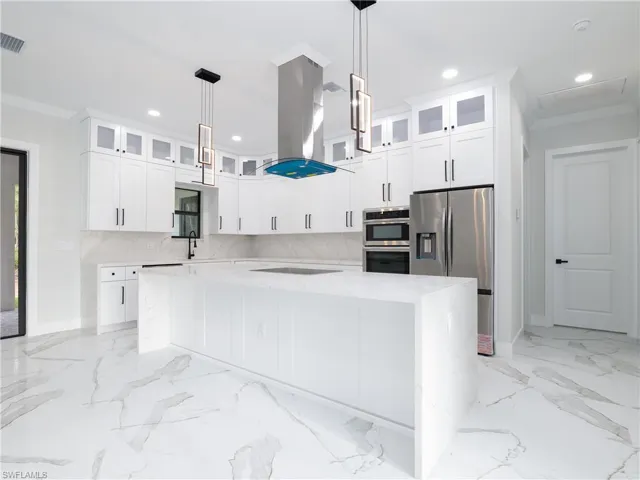 Kitchen with island exhaust hood, appliances with stainless steel finishes, tasteful backsplash, a spacious island, and light stone counters