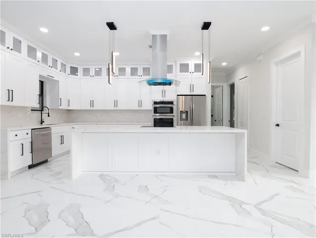 Kitchen featuring appliances with stainless steel finishes, decorative light fixtures, a center island, and backsplash