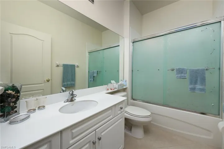 Full bathroom with tile floors, oversized vanity, combined bath / shower with glass door, and toilet