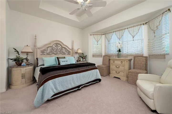 Bedroom featuring light carpet, ceiling fan, and a tray ceiling